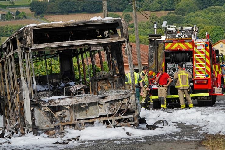 O autobús calcinado xunto a varios bombeiros durante o dispositivo de extinción do incendio, onde faleceu un bombeiro en prácticas 