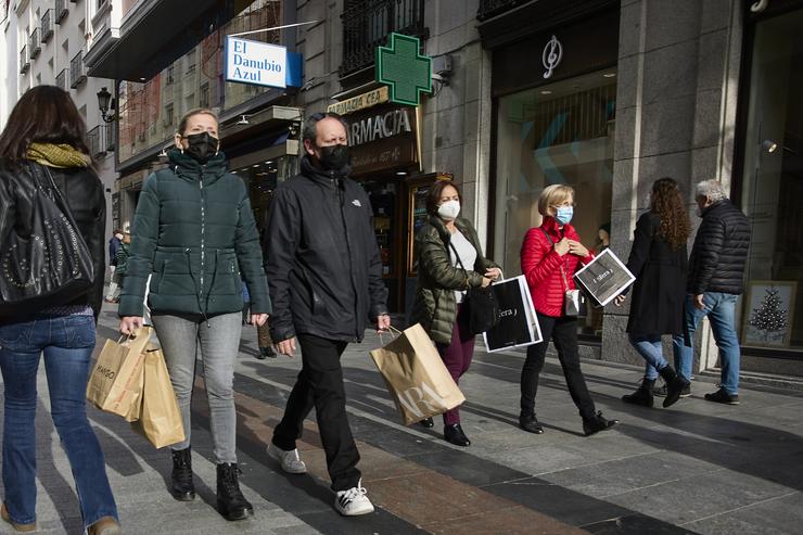 Varias persoas con bolsas pasean nunha rúa comercial 