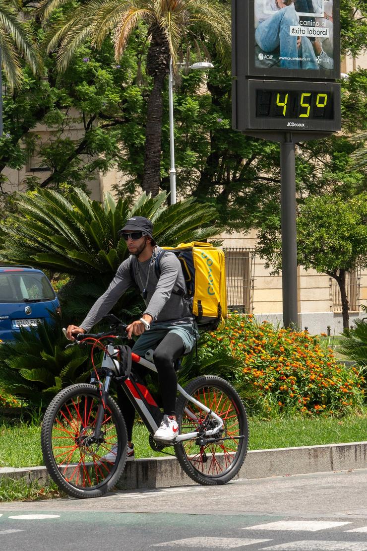 Un termómetro marca 45 graos ás 14:00 da tarde xunto a un traballador de Glovo en bicicleta, a 19 de xullo de 2024, en Sevilla, Andalucía.. Francisco J. Olmo - Europa Press / Europa Press